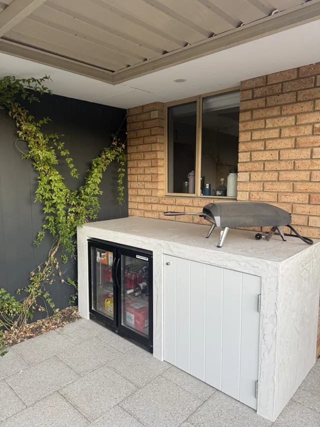 White barbecue & fridge surround: A pale textured surround with a barbecue, drinks fridge and white cabinetry.
